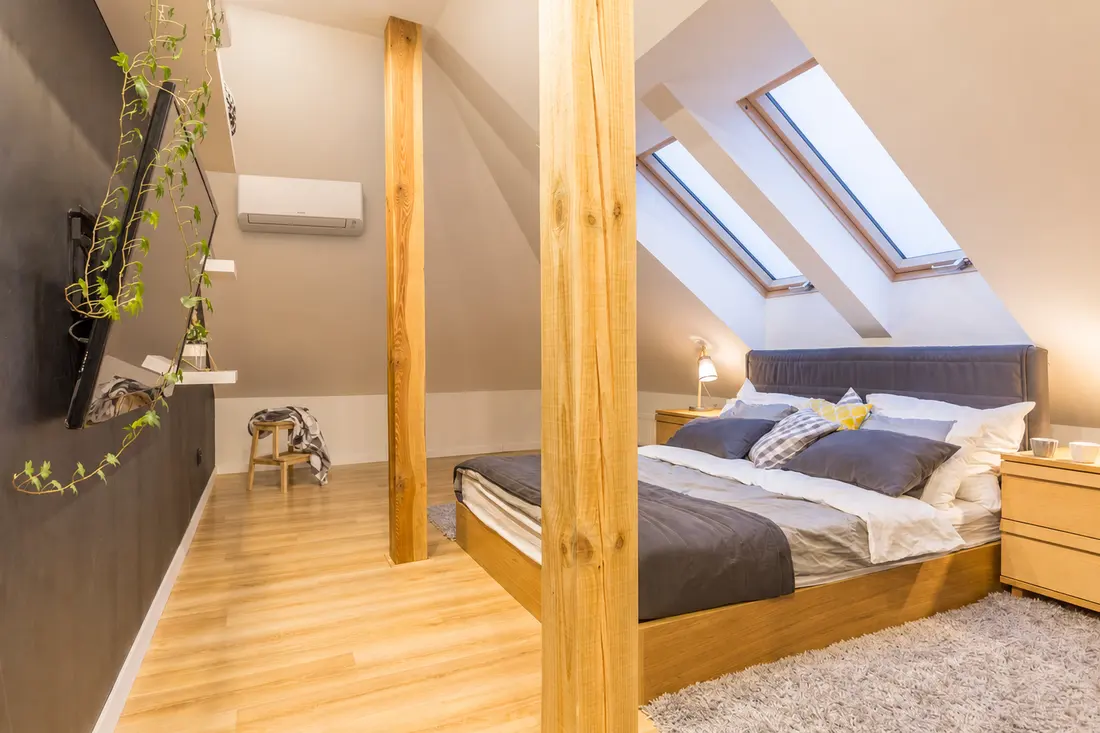 A loft conversion bedroom with roof windows and a wall-mounted air conditioning unit